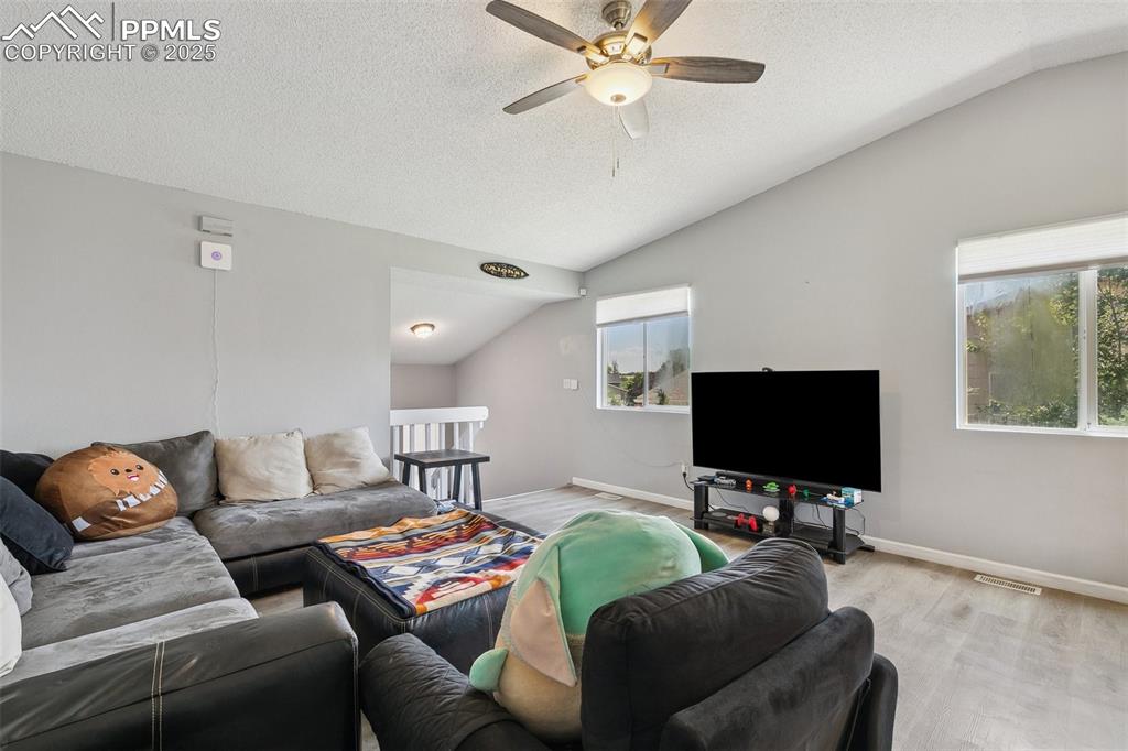 Living room featuring lofted ceiling, a ceiling fan, light wood-style flooring, and a textured ceiling