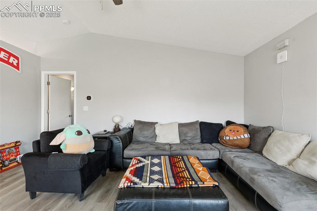 Living room with light wood-style flooring, vaulted ceiling, and ceiling fan