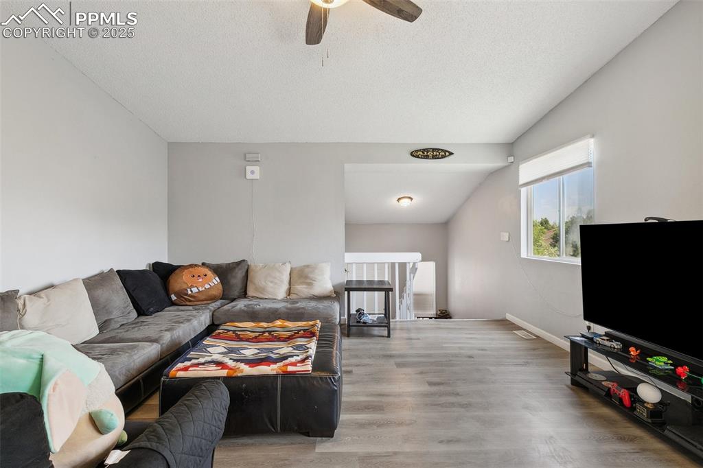 Living area featuring wood finished floors, ceiling fan, a textured ceiling, and lofted ceiling