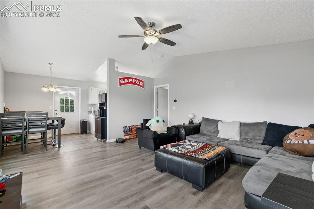 Living room with ceiling fan, light wood-type flooring, vaulted ceiling, and a chandelier