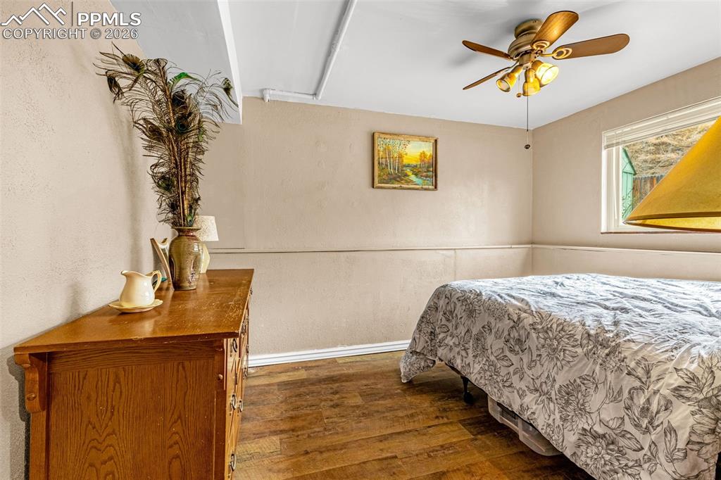 Bedroom featuring dark wood-style floors, ceiling fan, and a textured wall