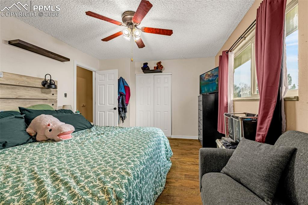 Bedroom with dark wood-style flooring, a closet, a ceiling fan, and a textured ceiling
