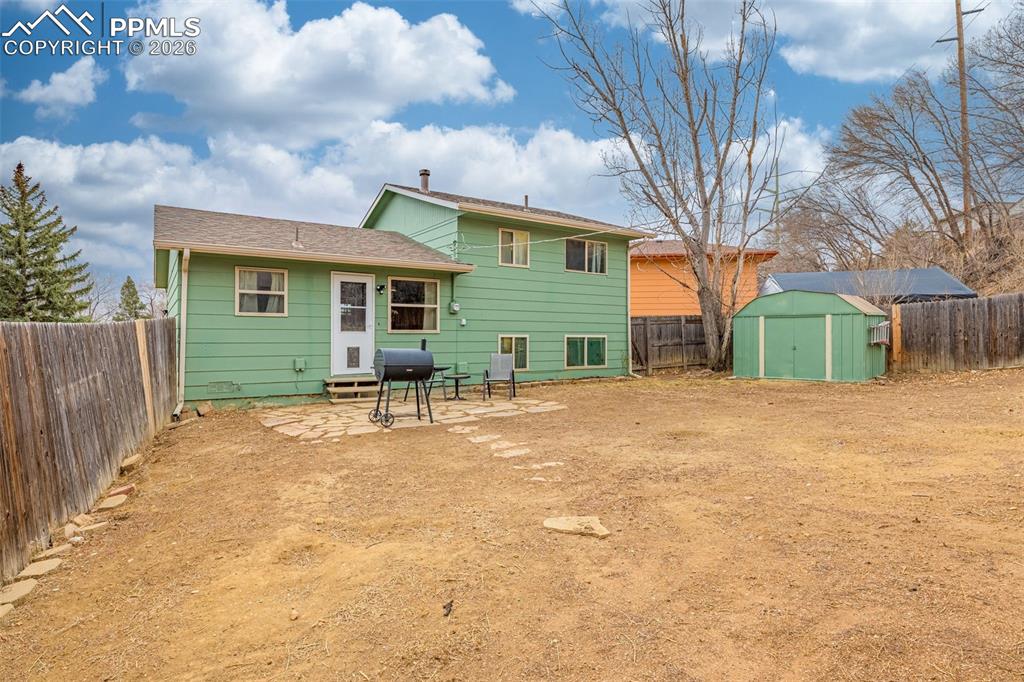 Back of house with a fenced backyard, a patio, and a storage unit