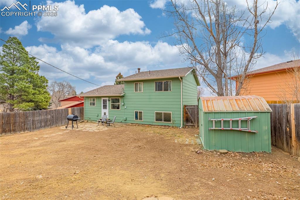 Back of house featuring a fenced backyard, a patio, and a shed