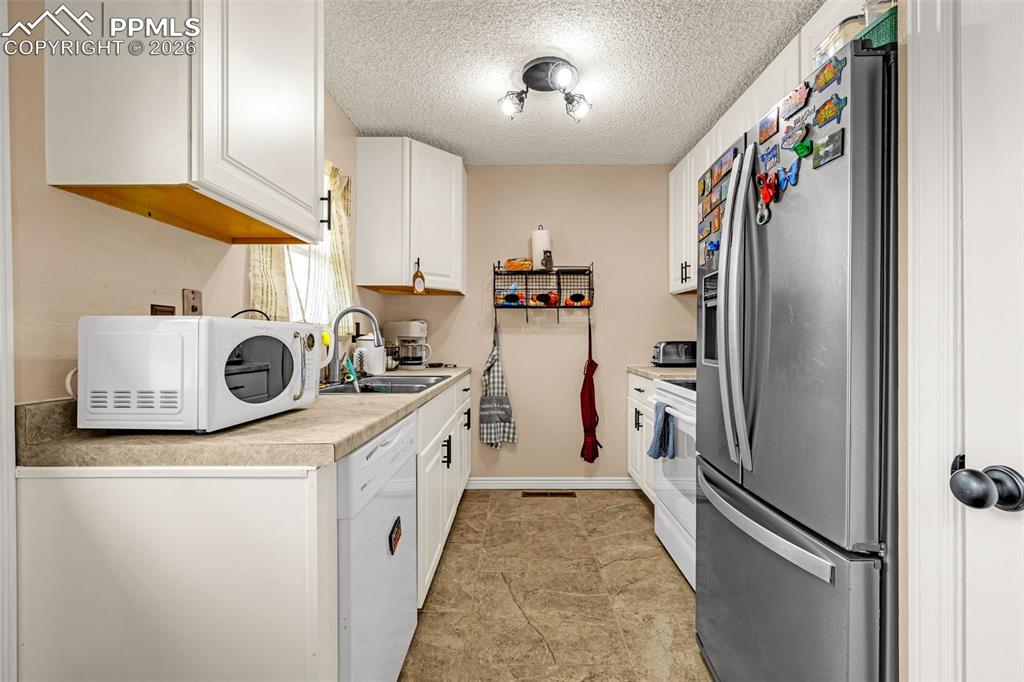 Kitchen with light countertops, white appliances, white cabinets, and a textured ceiling