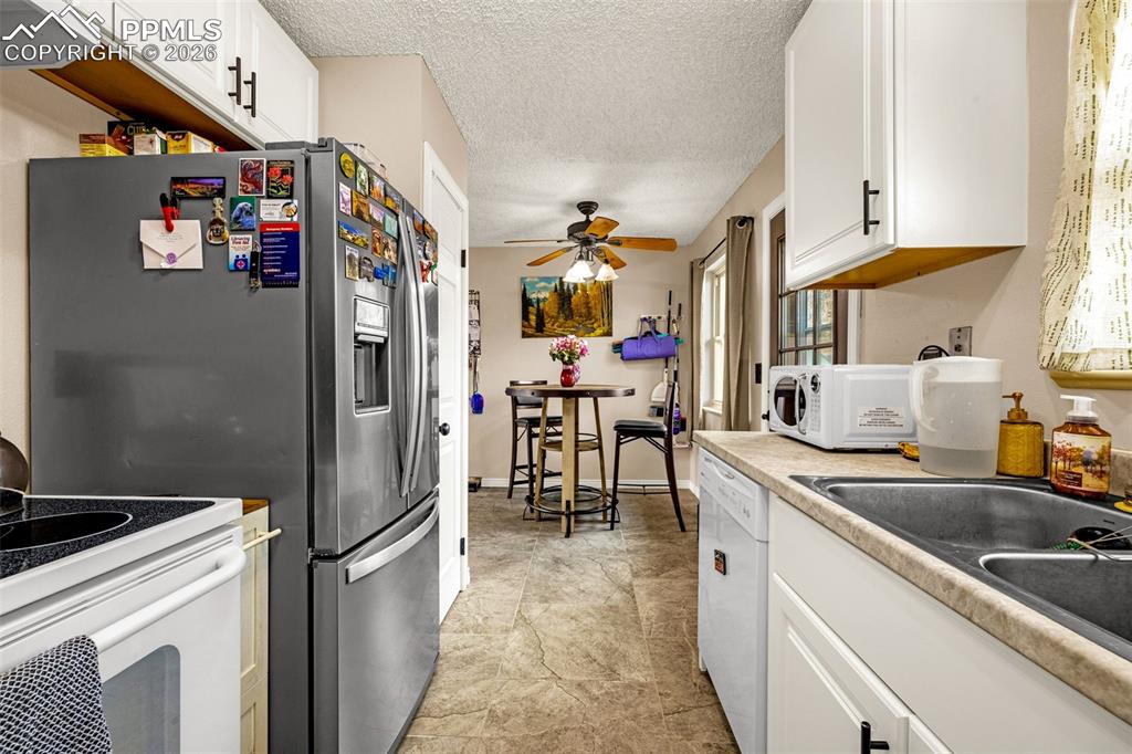 Kitchen featuring white cabinetry, a textured ceiling, white appliances, light countertops, and a ceiling fan