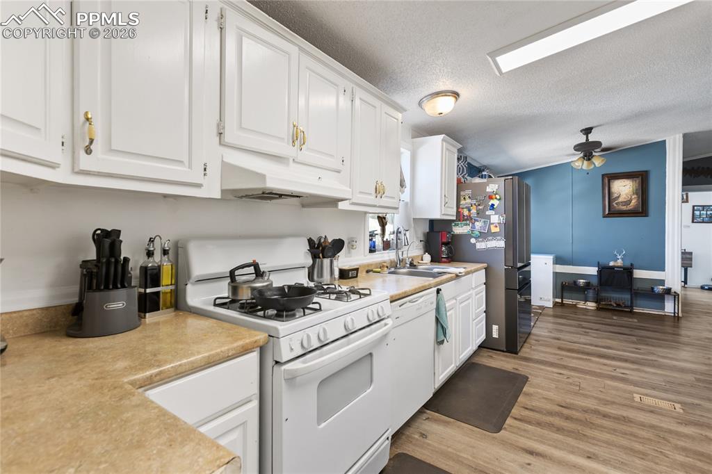 Kitchen has white appliances, white cabinetry, light countertops, and light wood flooring!