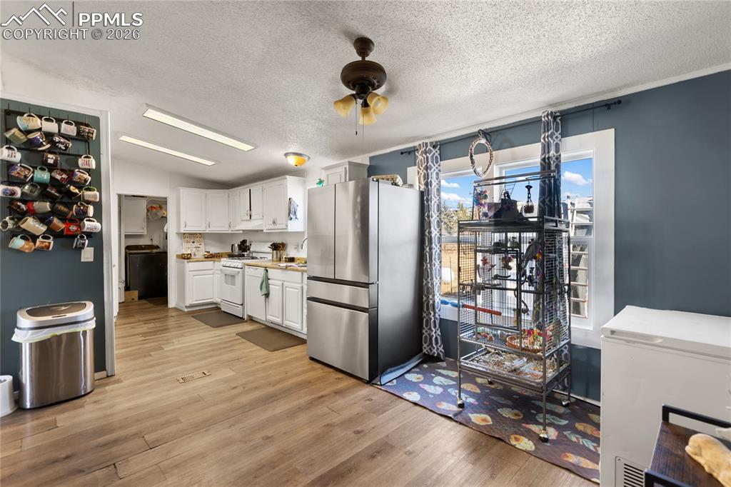The dining area overlooking the kitchen featuring freestanding refrigerator, white cabinetry, white gas range oven, light countertops, and light wood flooring!