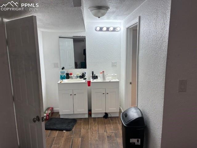 Bathroom with a textured wall, wood tiled floors, vanity, and a textured ceiling