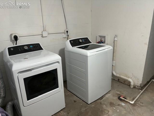 Laundry room featuring unfinished concrete floors, concrete block wall, and washer and clothes dryer