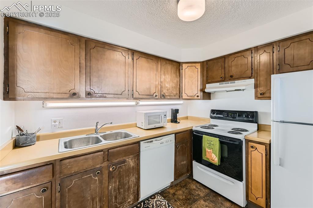 Kitchen featuring white appliances, under cabinet range hood, a textured ceiling, and light countertops
