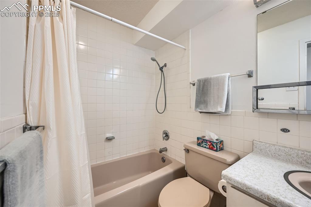 Bathroom with shower / bathtub combination with curtain, tile walls, and vanity