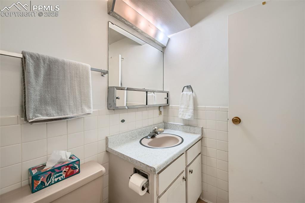 Half bathroom with tile walls, vanity, and a wainscoted wall