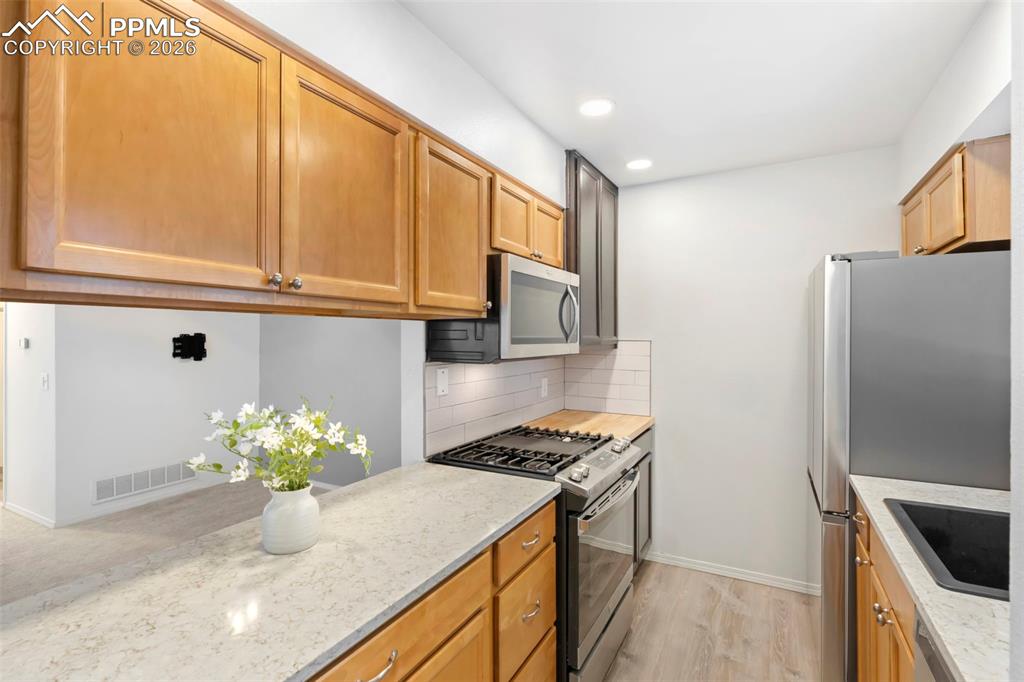 Kitchen featuring appliances with stainless steel finishes, decorative backsplash, light stone countertops, light wood-style luxury vinyl floors, and recessed lighting