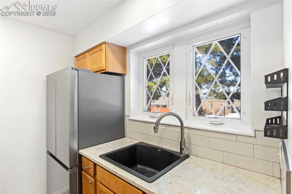 Kitchen with stainless steel refrigerator, light quartz counters, wood cabinetry, and tile backsplash