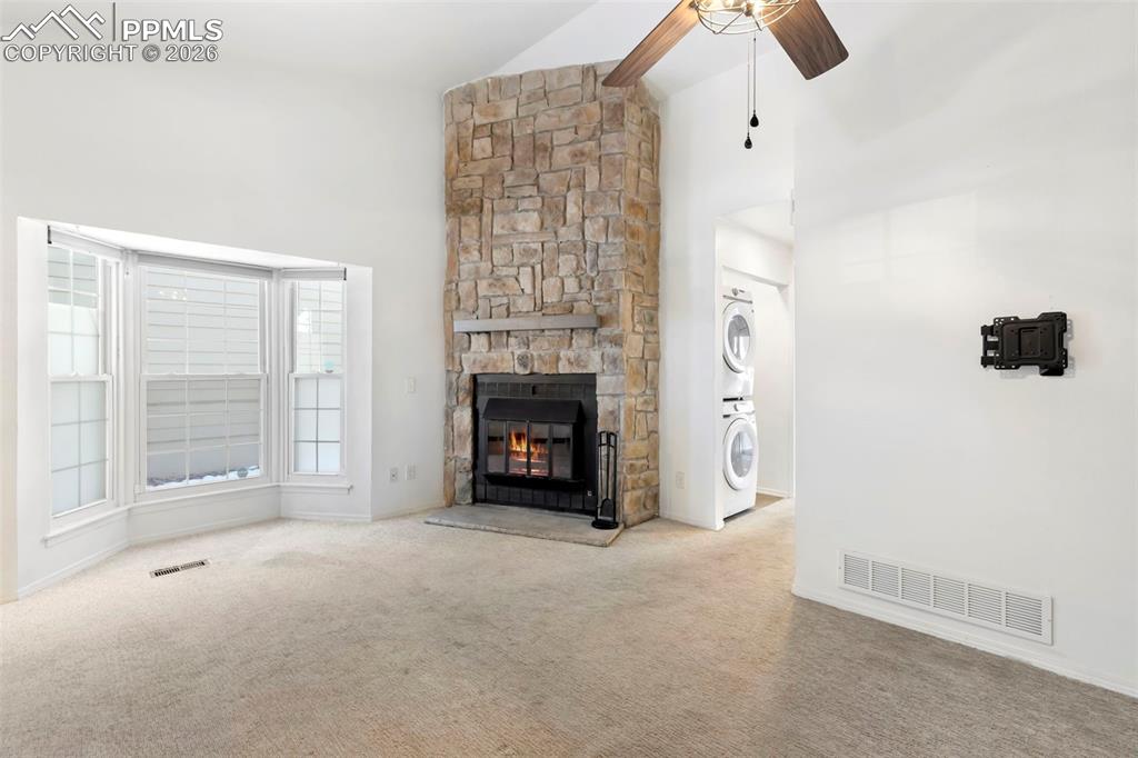 Living room featuring high vaulted ceiling, a stone fireplace, ceiling fan, and carpet floors