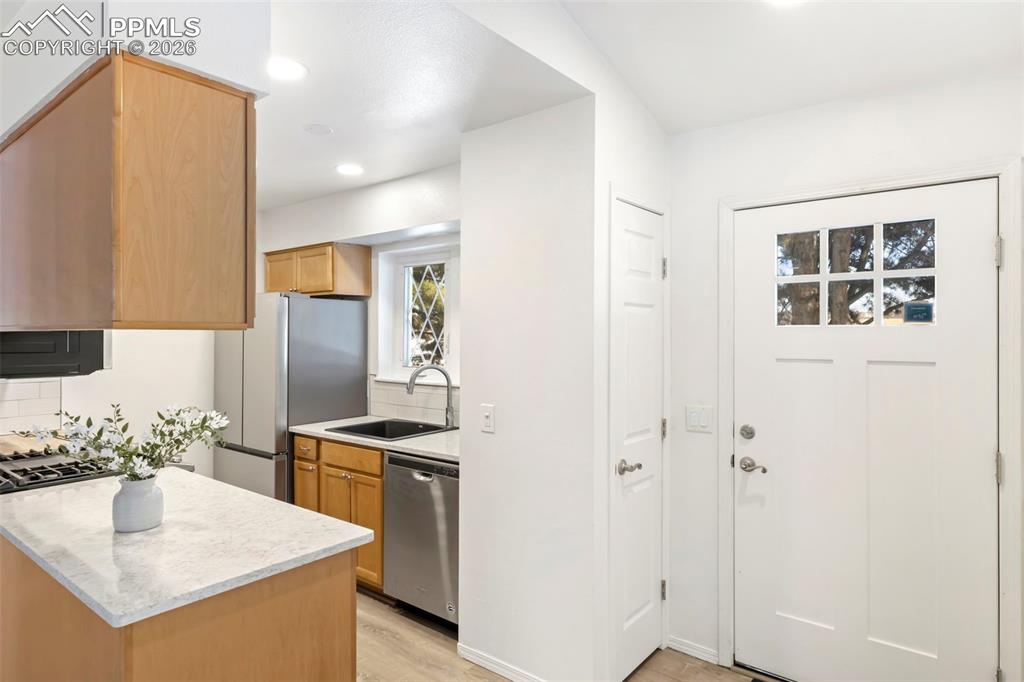 Kitchen with stainless steel appliances, decorative backsplash, recessed lighting, light wood-style flooring, and light stone counters
