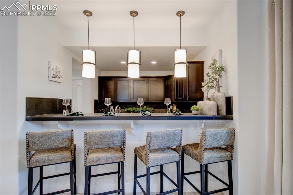 Kitchen with dark brown cabinetry, pendant lighting, a kitchen breakfast bar, dark countertops, and recessed lighting