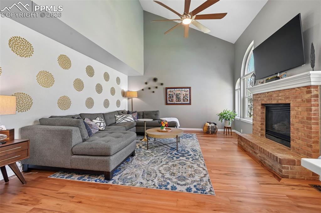 Living room with light wood-type flooring, vaulted ceiling, a ceiling fan, and a fireplace