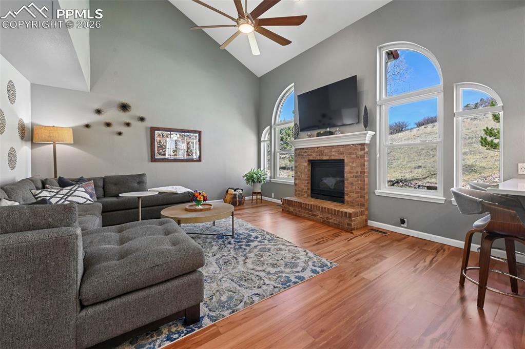 Living area featuring wood finished floors, a fireplace, vaulted ceiling, and a ceiling fan