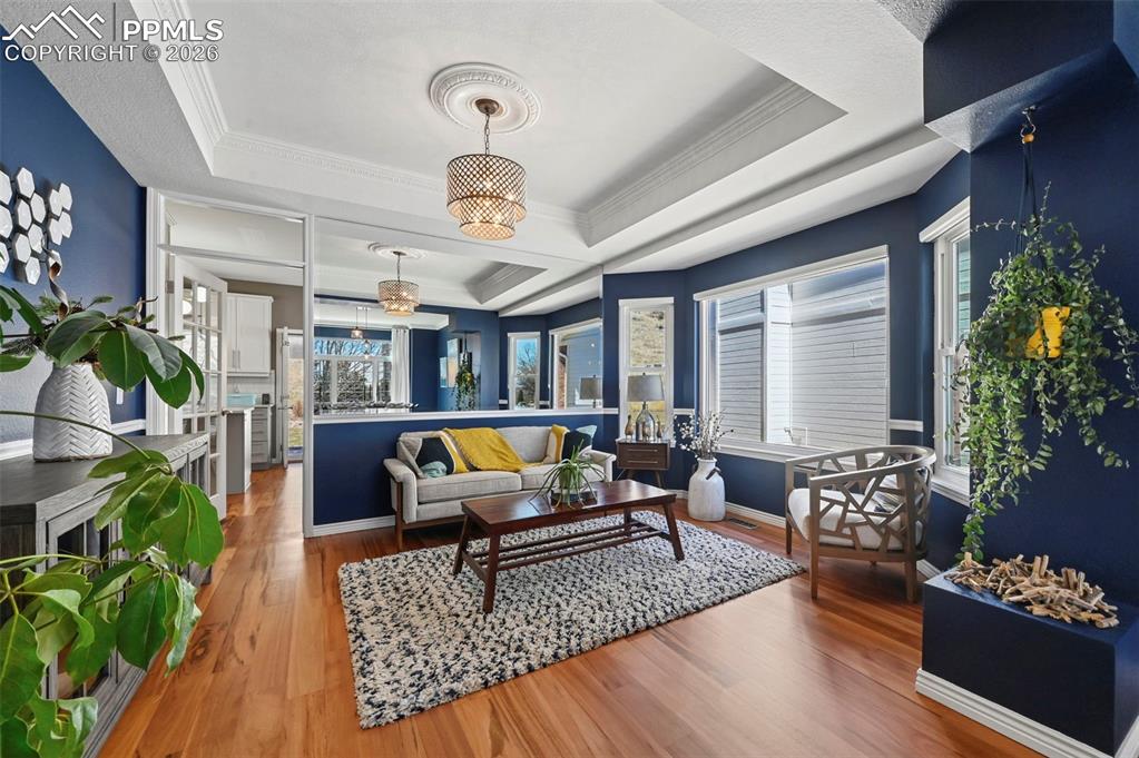 Living room with wood finished floors, a raised ceiling, ornamental molding, and suspended lighting