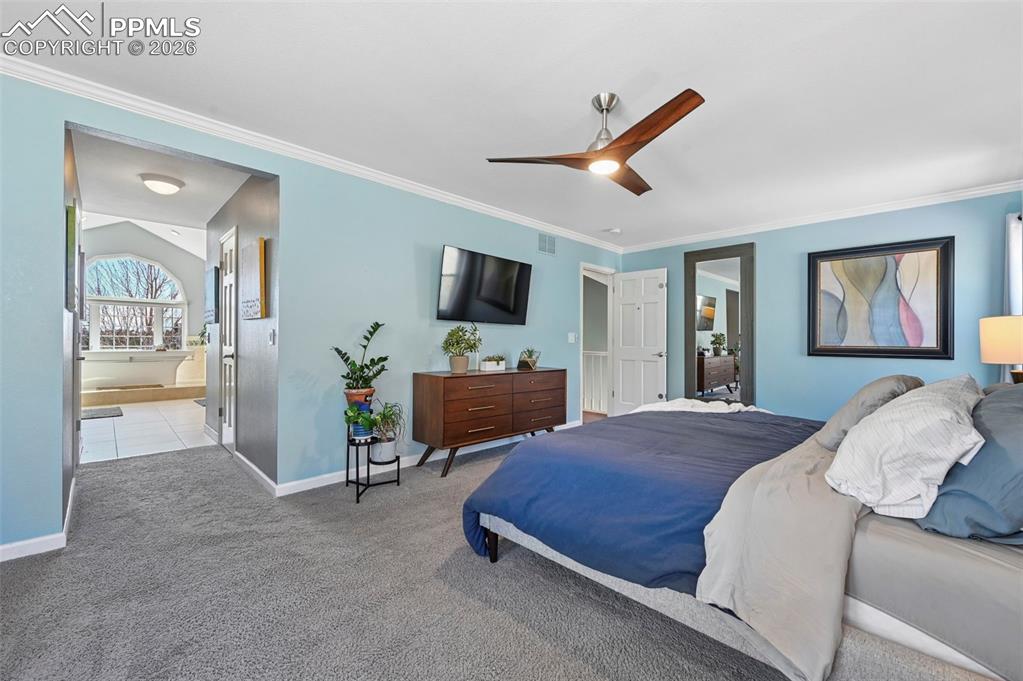 Bedroom with ensuite bath, crown molding, carpet flooring, and a ceiling fan
