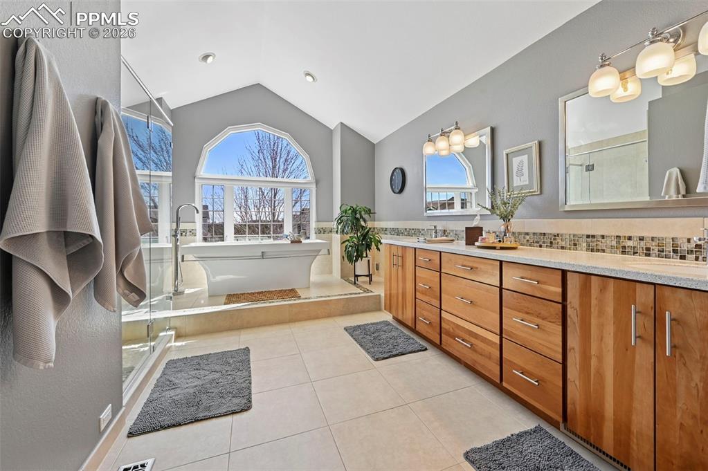 Bathroom with double vanity, light tile patterned floors, a freestanding bath, a stall shower, and vaulted ceiling