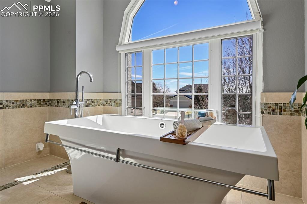 Bathroom featuring a wainscoted wall, tile walls, a freestanding tub, and light tile patterned floors