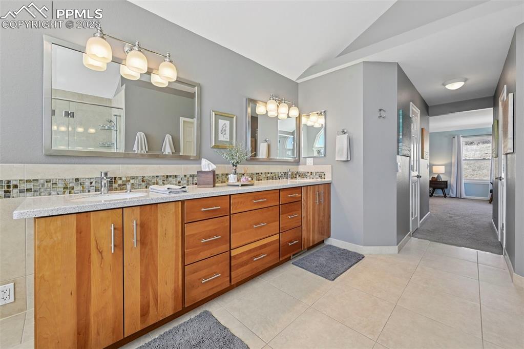 Bathroom featuring double vanity, vaulted ceiling, light tile patterned floors, and an enclosed shower