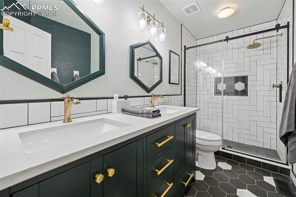 Bathroom with double vanity, dark tile patterned floors, a shower stall, a textured wall, and tile walls