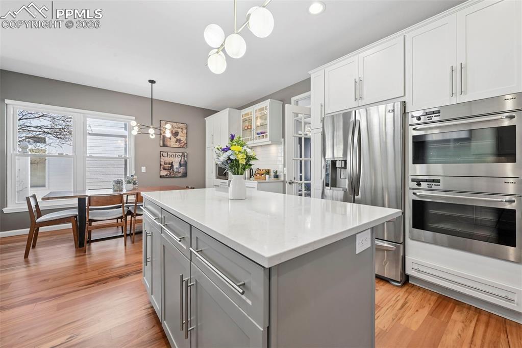 Kitchen featuring stainless steel appliances, light wood-type flooring, glass fronted cabinets, a chandelier, and a center island
