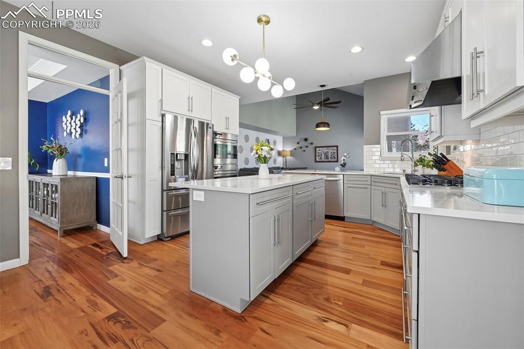 Kitchen featuring a kitchen island, backsplash, stainless steel appliances, light stone counters, and light wood-style flooring