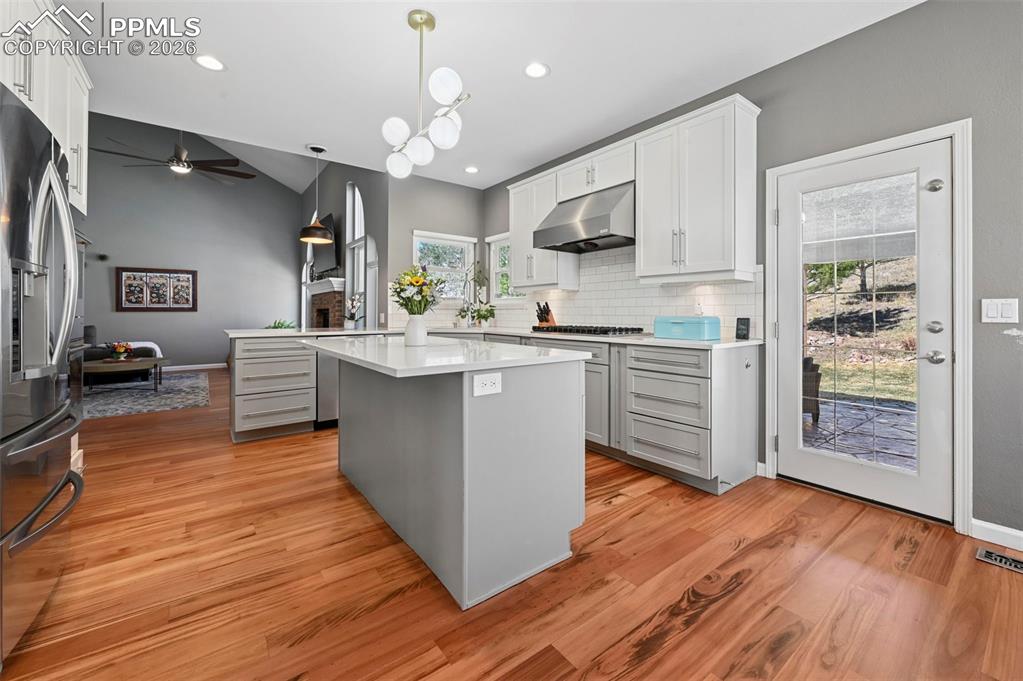 Kitchen with a island, a ceiling fan, stainless steel fridge, tasteful backsplash, and wood floors