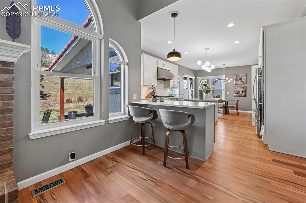 Kitchen featuring a breakfast bar area, a peninsula, suspended lighting, white cabinetry, and light wood-type flooring