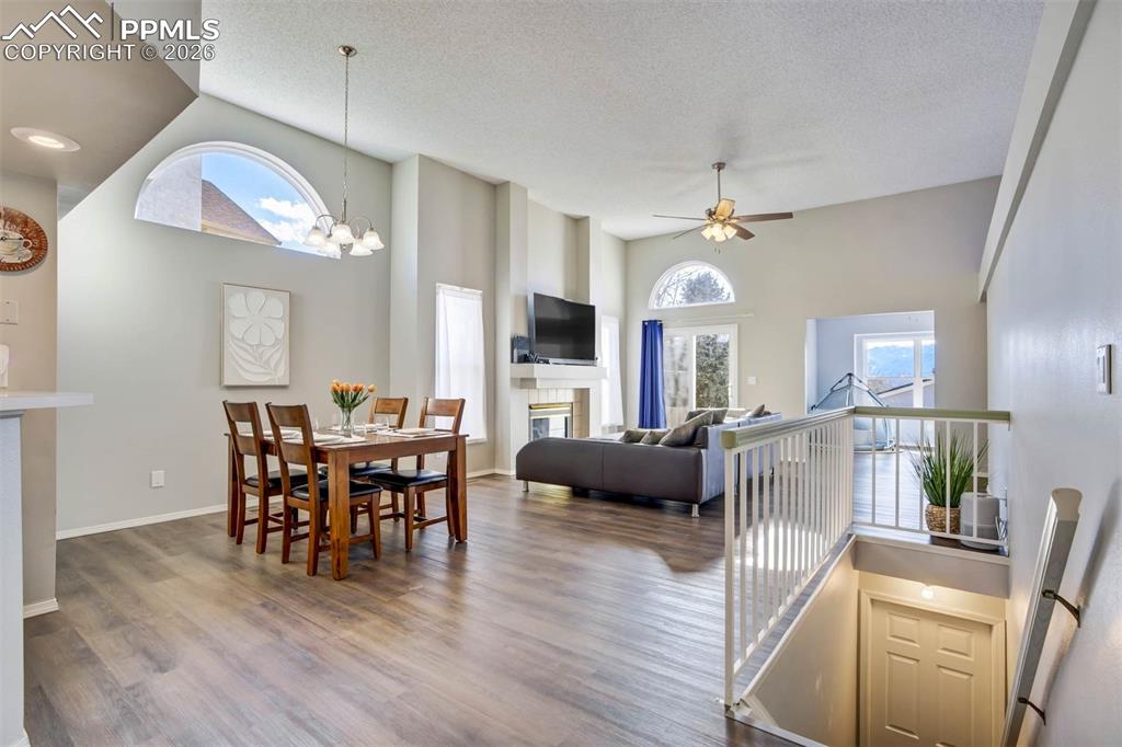 Dining area featuring a ceiling fan, a glass covered fireplace, a chandelier, dark wood-type flooring, and a high textured ceiling