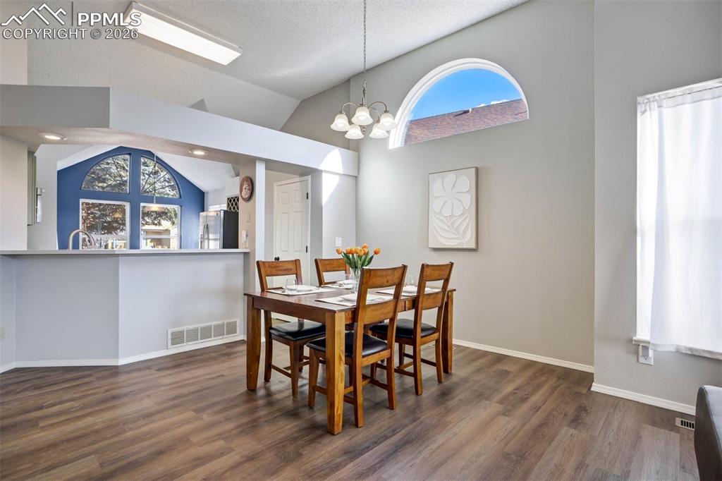 Dining space with lofted ceiling, hanging lights, and dark wood-style floors