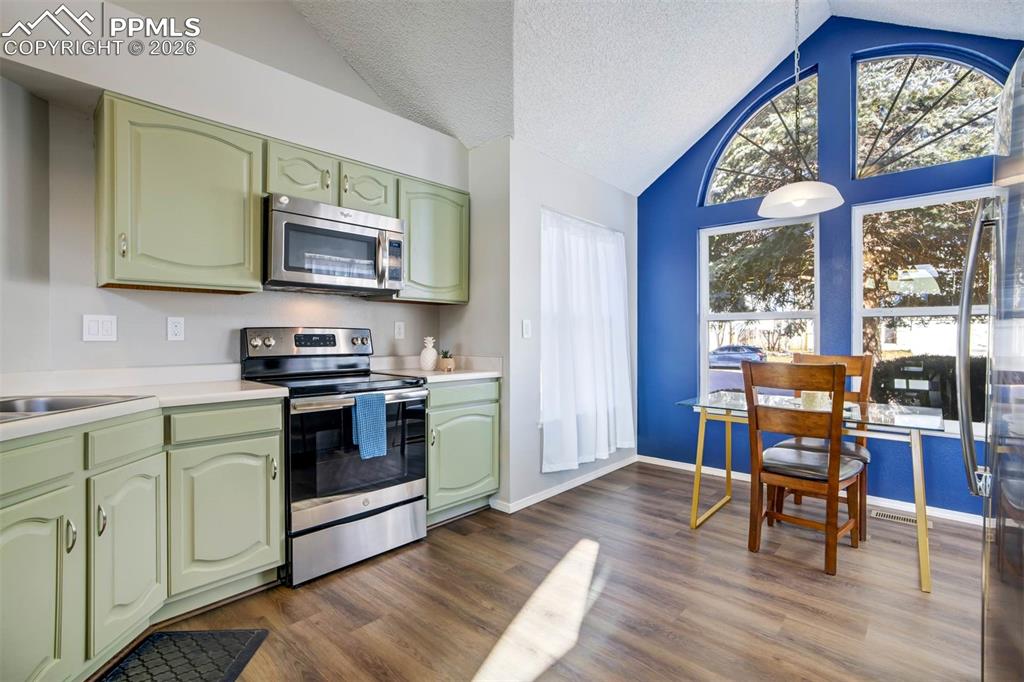 Kitchen featuring green cabinets, stainless steel appliances, light countertops, and dark wood-style floors