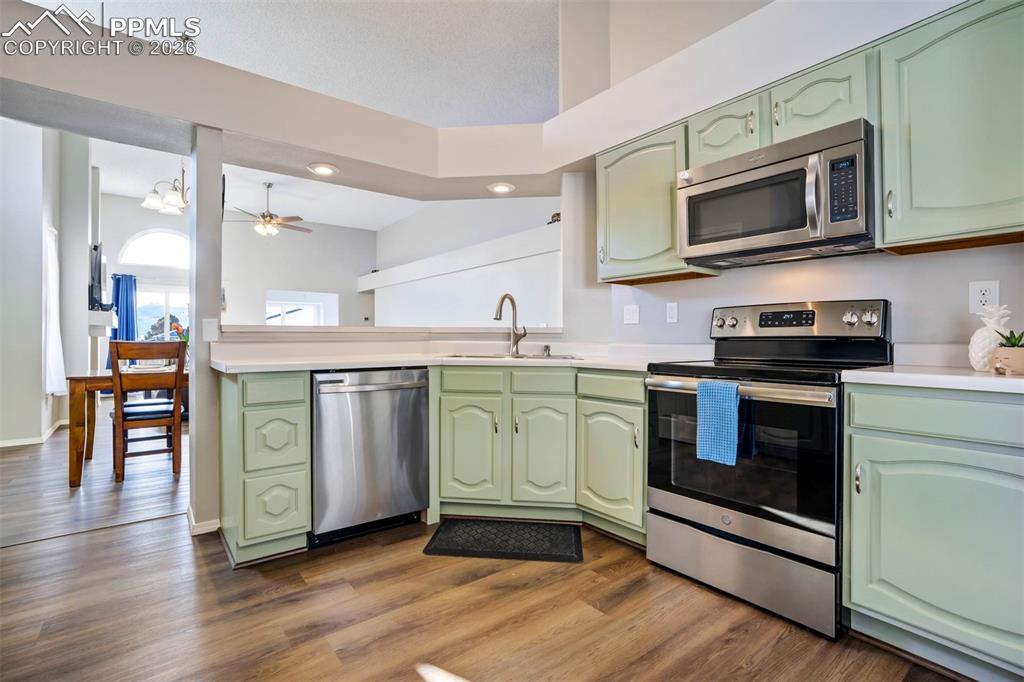 Kitchen featuring green cabinetry, stainless steel appliances, light countertops, dark wood-type flooring, and recessed lighting