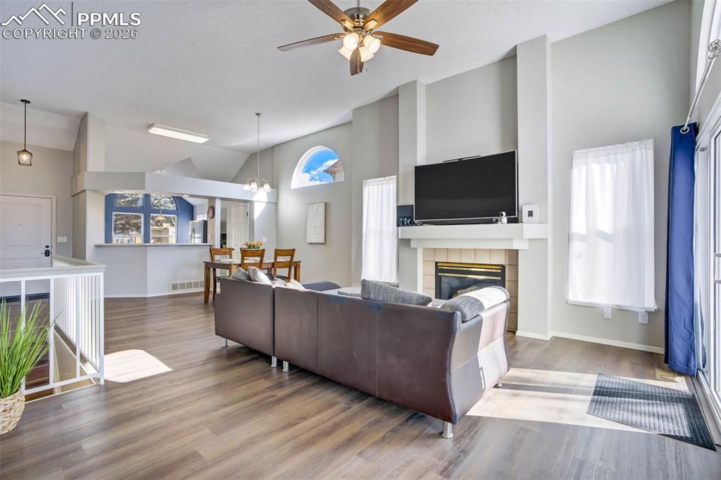 Living area with vaulted ceiling, a ceiling fan, wood finished floors, a tile fireplace, and hanging lights