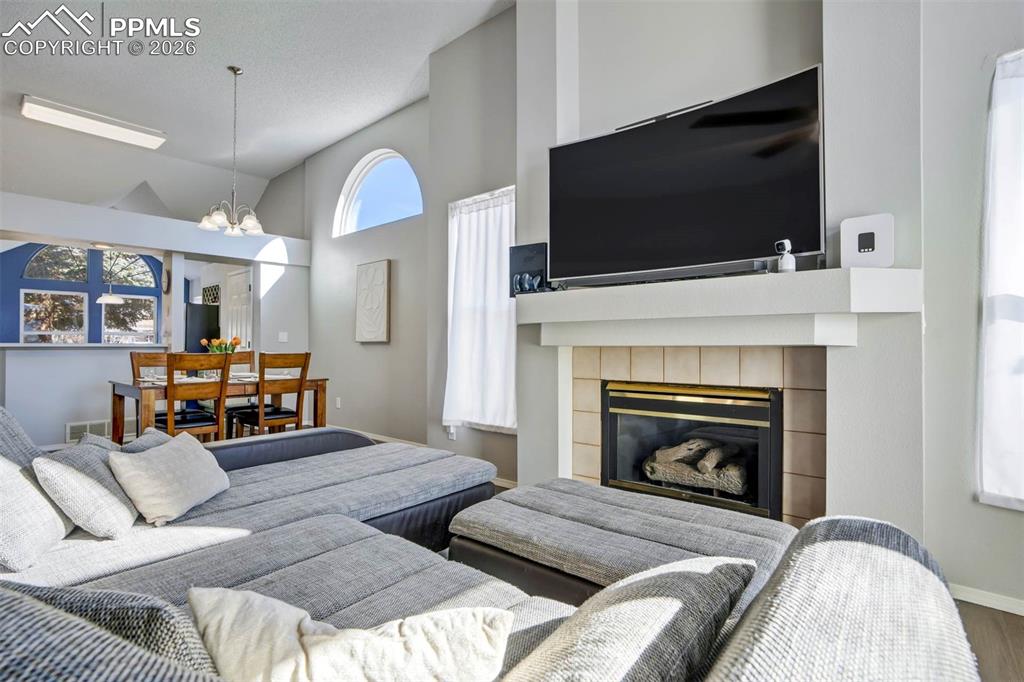 Living room with lofted ceiling, suspended lighting, and a fireplace