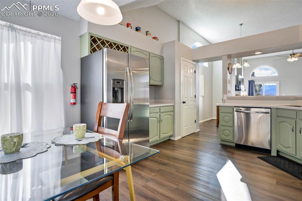 Kitchen with green cabinets, light countertops, stainless steel appliances, a high textured ceiling, and dark wood finished floors