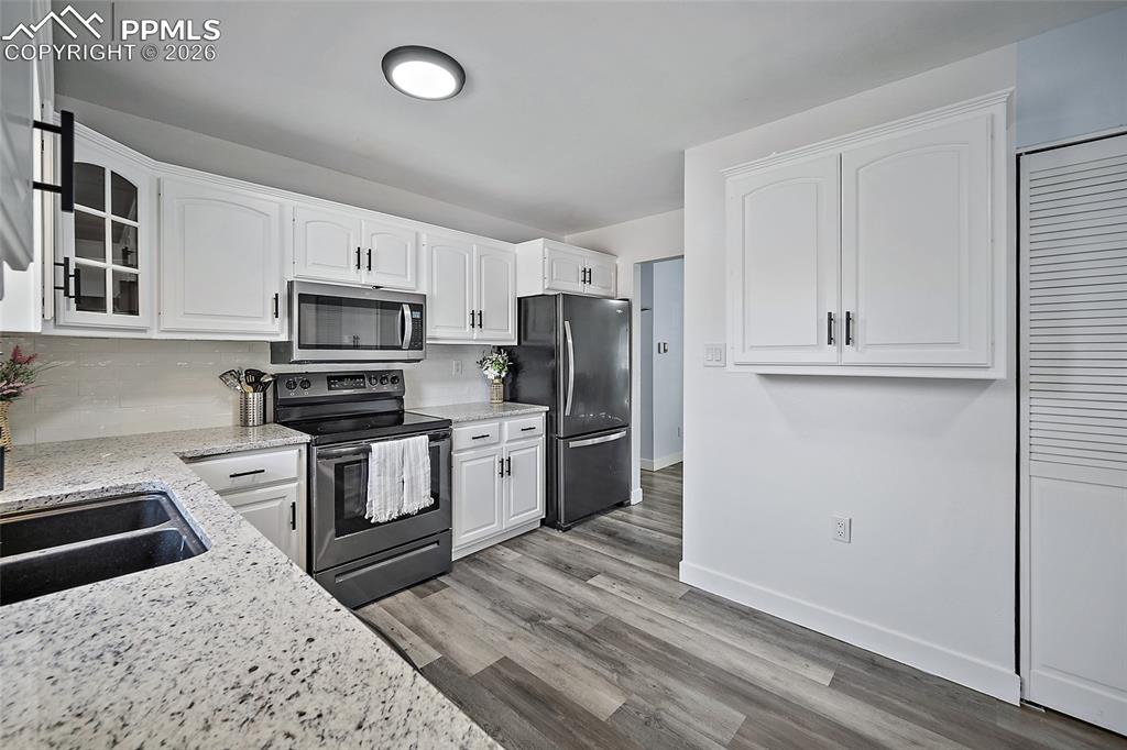 Kitchen featuring stainless steel appliances with white cabinetry and granite countertops