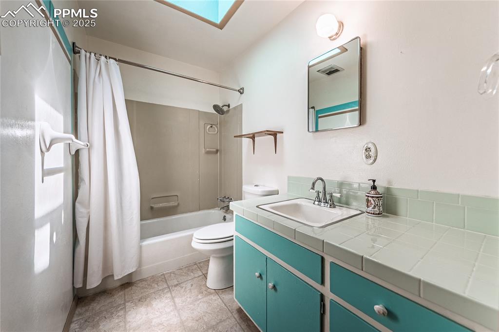 Bathroom featuring a skylight, shower / bathtub combination with curtain, vanity, and light tile patterned floors