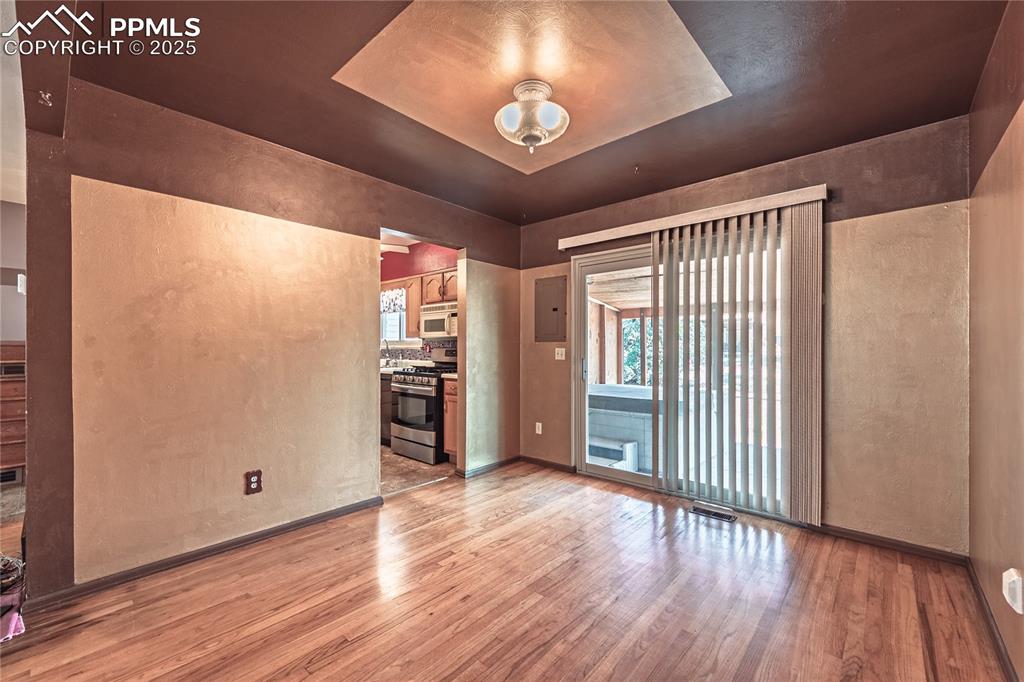 Spare room with a textured wall, light wood-style flooring, a tray ceiling, and electric panel