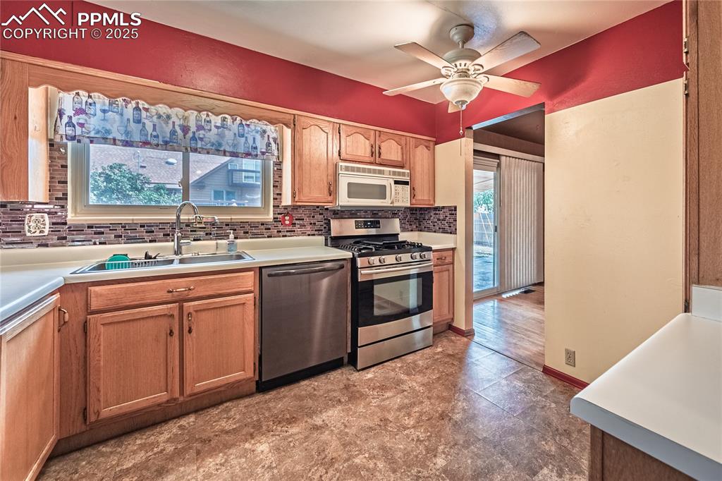 Kitchen featuring stainless steel appliances, backsplash, light countertops, a ceiling fan, and light brown cabinets