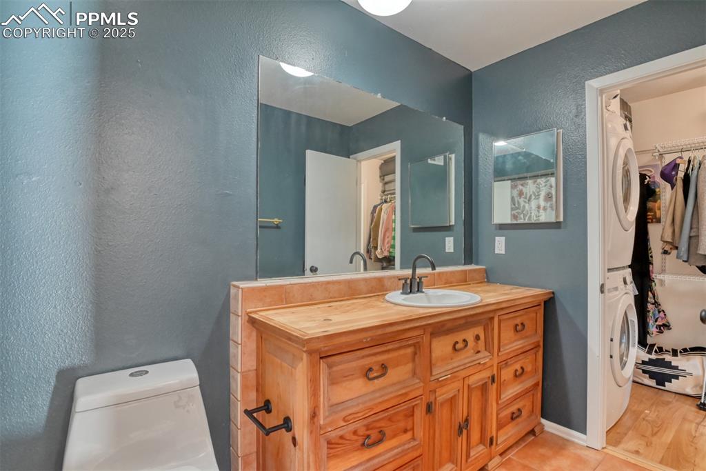 Bathroom featuring a spacious closet, a textured wall, vanity, stacked washer / dryer, and light tile patterned flooring