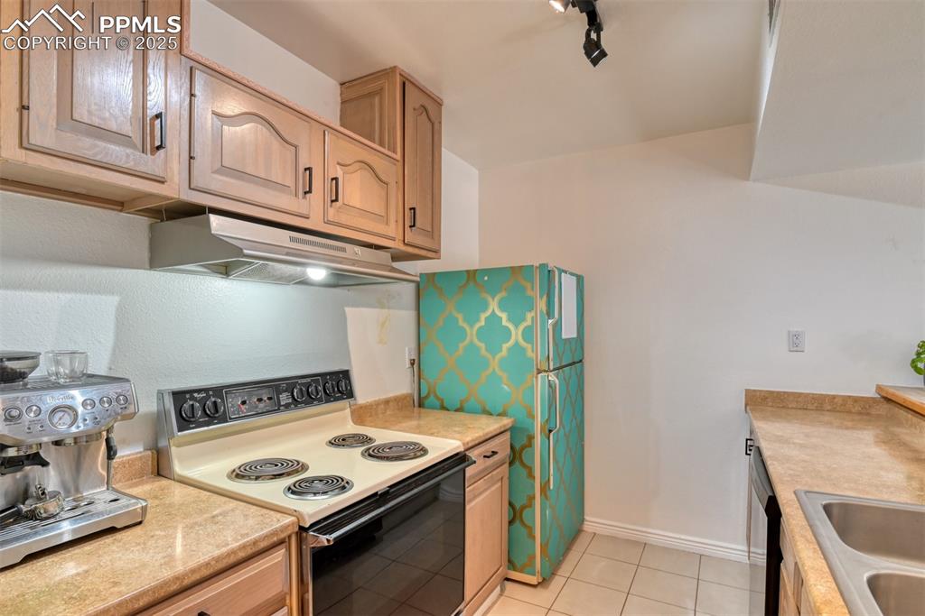 Kitchen with electric stove, light countertops, under cabinet range hood, light tile patterned floors, and dishwasher