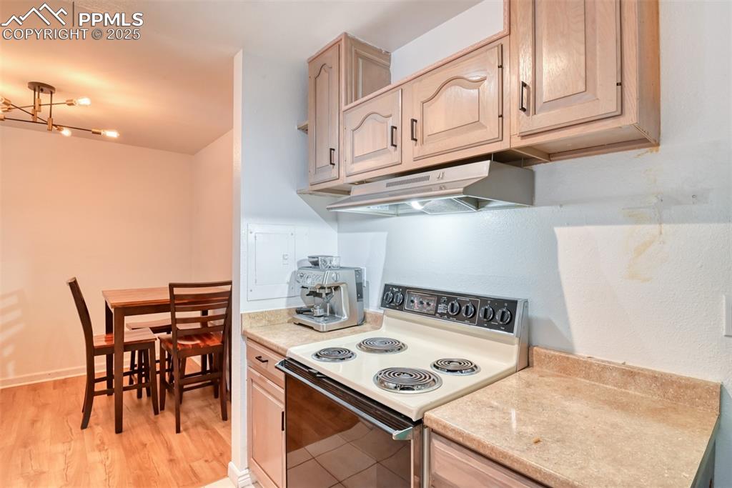 Kitchen with electric stove, light countertops, under cabinet range hood, and light brown cabinetry