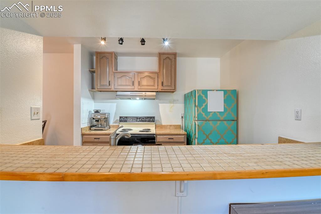 Kitchen featuring range with electric stovetop, freestanding refrigerator, tile counters, a textured wall, and under cabinet range hood