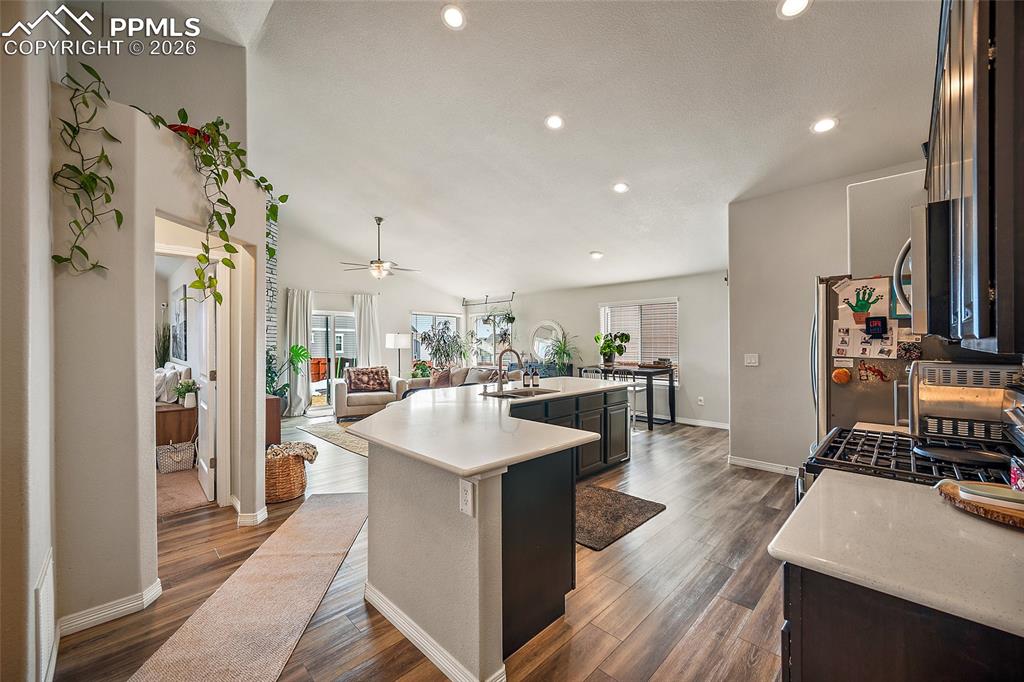 Kitchen with open floor plan, an island with sink, gas stove, dark wood-type flooring, and stainless steel microwave